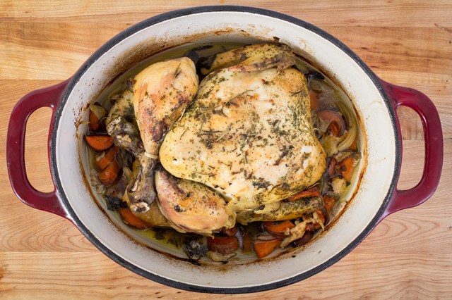 Areal view of a whole chicken in a slow cooker pot surrounded by vegetables. 